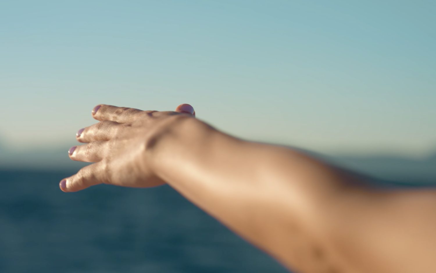 A hand trailing through the surface of the sea, first light
